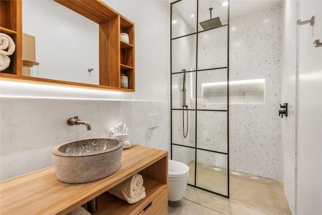 bathroom with a tile shower, tile patterned flooring, toilet, vanity, and tile walls