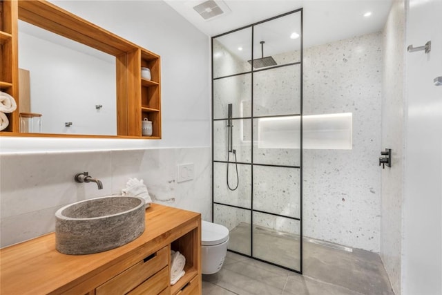 bathroom with a tile shower, toilet, decorative backsplash, vanity, and tile walls