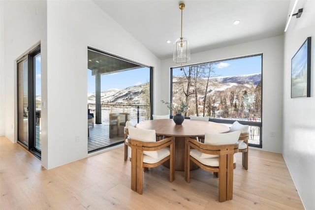 dining room with a mountain view, vaulted ceiling, and light wood-type flooring