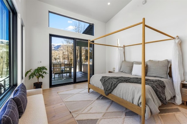 bedroom with access to exterior, light hardwood / wood-style floors, and high vaulted ceiling