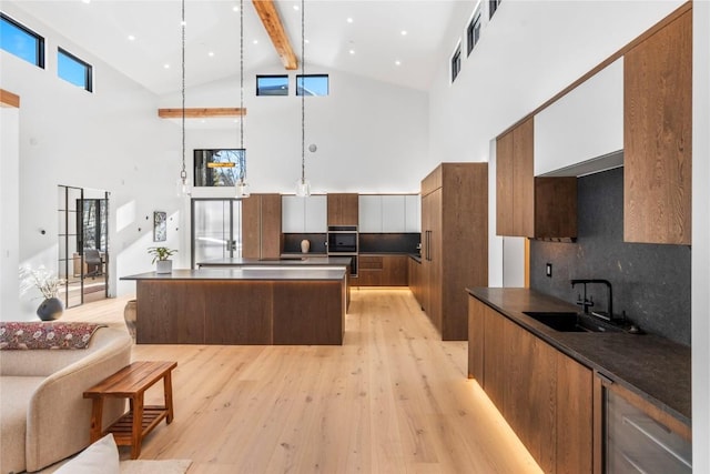 kitchen featuring decorative light fixtures, high vaulted ceiling, tasteful backsplash, and sink