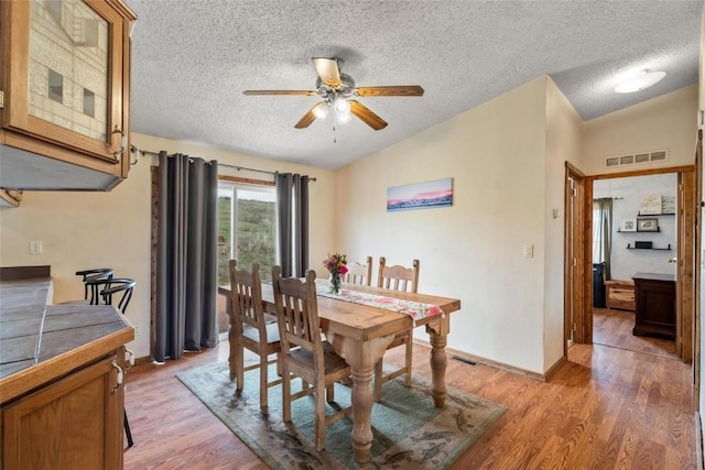 dining area with a textured ceiling, ceiling fan, light hardwood / wood-style flooring, and lofted ceiling