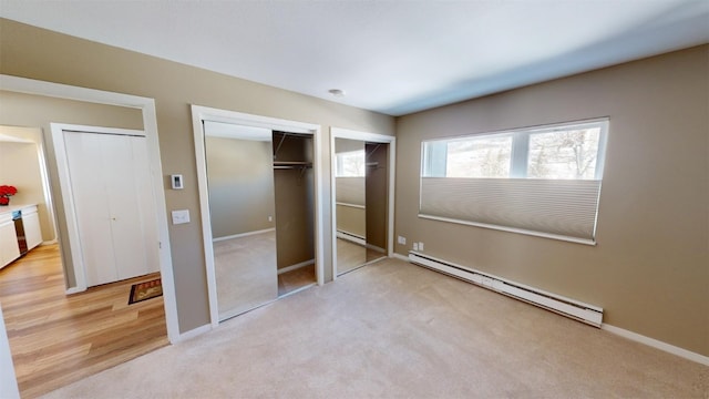 unfurnished bedroom featuring light colored carpet, baseboard heating, and multiple closets