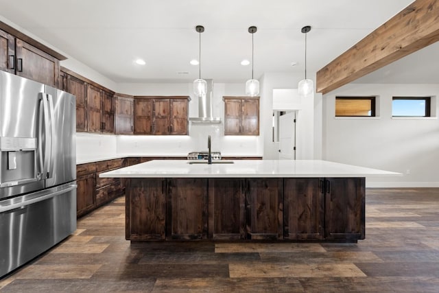 kitchen with wall chimney exhaust hood, stainless steel fridge with ice dispenser, beamed ceiling, decorative light fixtures, and a kitchen island with sink