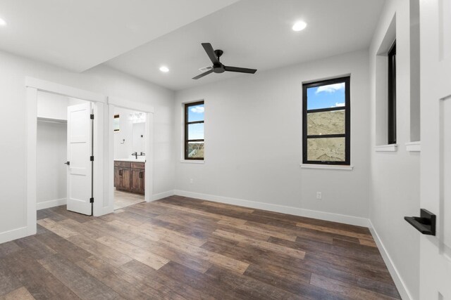 unfurnished bedroom with ceiling fan, dark wood-type flooring, connected bathroom, and multiple windows