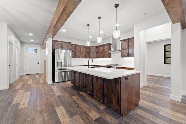 kitchen featuring stainless steel fridge, sink, wall chimney range hood, pendant lighting, and an island with sink