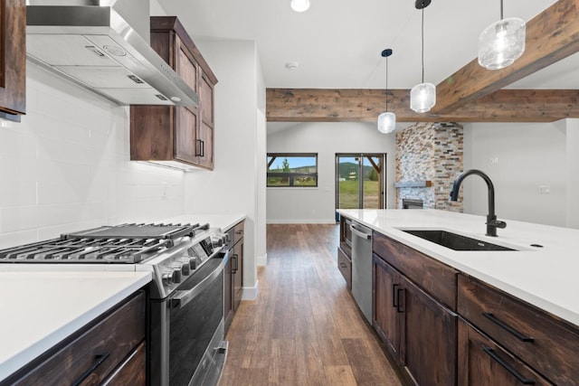 kitchen featuring stainless steel appliances, sink, wall chimney range hood, pendant lighting, and beam ceiling