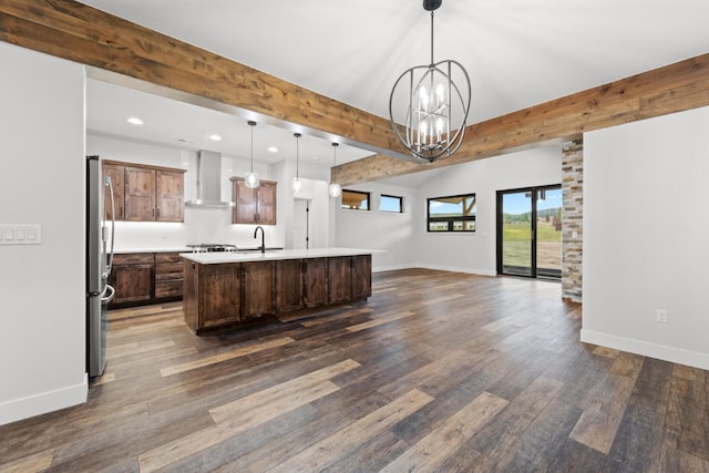 kitchen featuring a center island with sink, wall chimney exhaust hood, stainless steel fridge, beamed ceiling, and decorative light fixtures