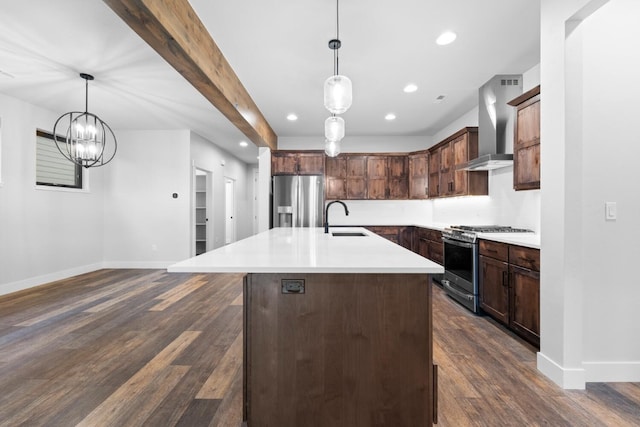 kitchen featuring appliances with stainless steel finishes, wall chimney exhaust hood, sink, a center island with sink, and hanging light fixtures