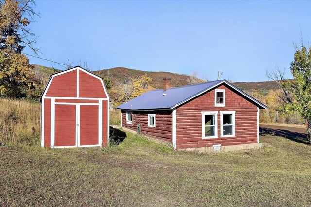 back of house with a lawn, a mountain view, and a shed