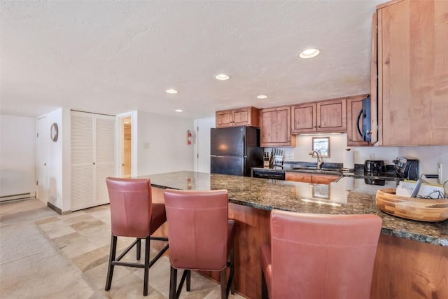 kitchen featuring black refrigerator, sink, dark stone countertops, a kitchen bar, and kitchen peninsula