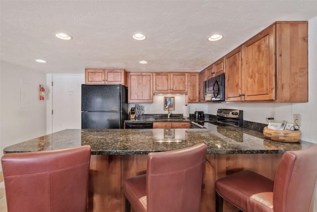 kitchen with sink, dark stone counters, a kitchen bar, and black appliances