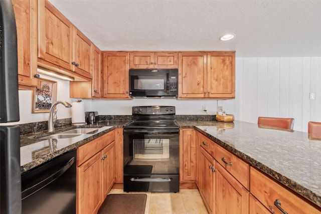 kitchen with sink, dark stone countertops, a kitchen bar, light tile patterned floors, and black appliances