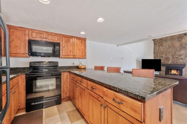 kitchen with a stone fireplace, a breakfast bar area, dark stone counters, and black appliances