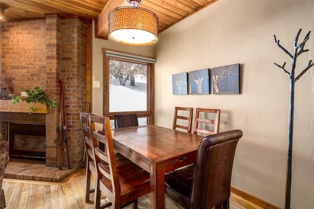 dining space with wooden ceiling, a fireplace, and light wood-style floors