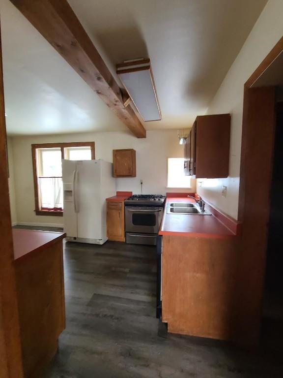 kitchen featuring sink, dark wood-type flooring, beam ceiling, stainless steel range with gas stovetop, and white fridge with ice dispenser