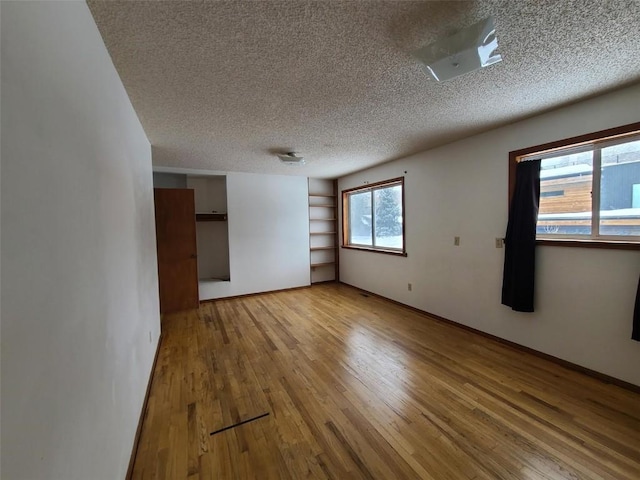 empty room featuring light hardwood / wood-style flooring, built in features, and a textured ceiling