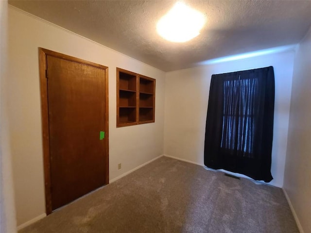 empty room with built in shelves, a textured ceiling, and dark colored carpet