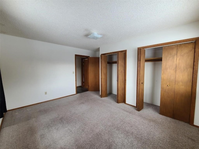 unfurnished bedroom with light carpet, a textured ceiling, and multiple closets