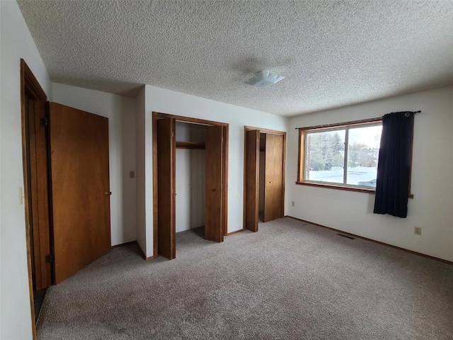 unfurnished bedroom featuring multiple closets, light carpet, and a textured ceiling