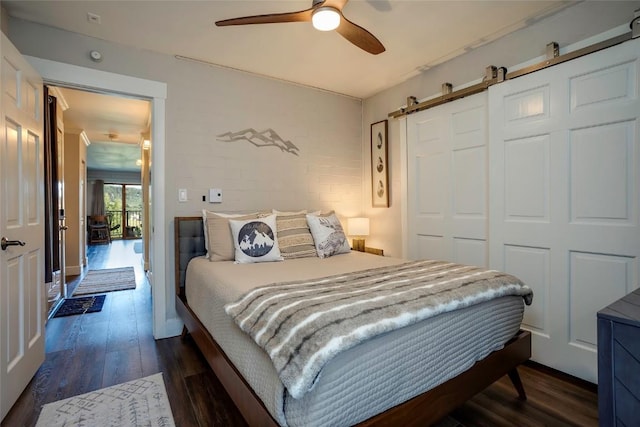 bedroom with a barn door, ceiling fan, a closet, and dark wood-type flooring