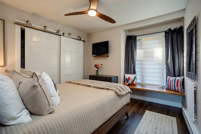 bedroom featuring ceiling fan, a barn door, dark wood-type flooring, and a closet