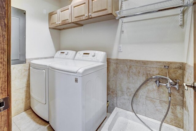 clothes washing area featuring washer and dryer, light tile patterned floors, cabinets, and tile walls