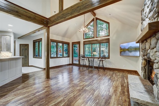 unfurnished living room with beam ceiling, a stone fireplace, wood-type flooring, and a notable chandelier