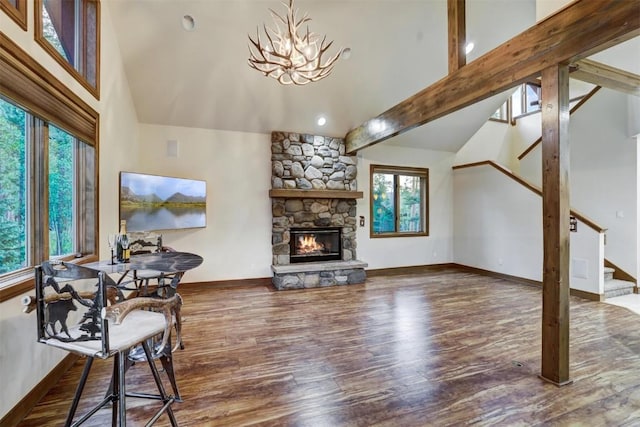 living room featuring dark hardwood / wood-style floors, beam ceiling, a stone fireplace, and a chandelier