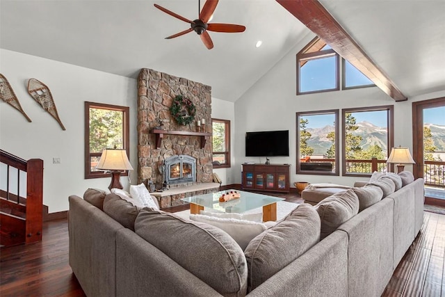 living room with a ceiling fan, dark wood-type flooring, a stone fireplace, high vaulted ceiling, and beam ceiling