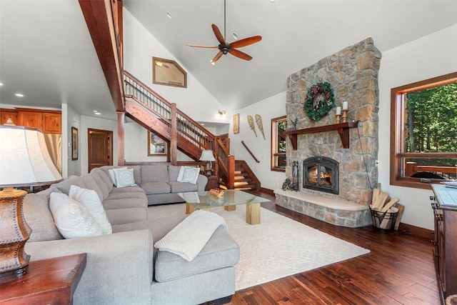 living room featuring dark wood finished floors, stairway, a stone fireplace, high vaulted ceiling, and baseboards