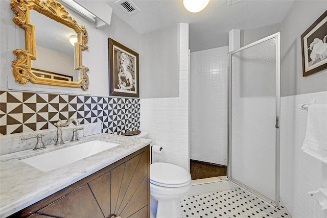 bathroom with vanity, a shower with door, tile walls, and toilet