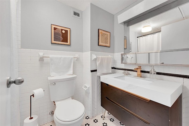 bathroom with tile walls, vanity, tile patterned floors, and toilet