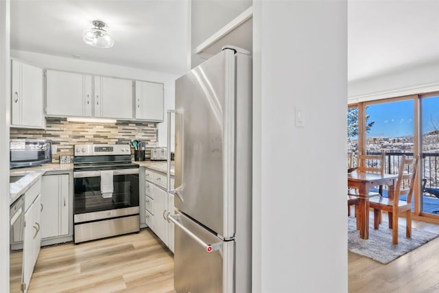 kitchen featuring light wood-type flooring, appliances with stainless steel finishes, tasteful backsplash, and white cabinetry