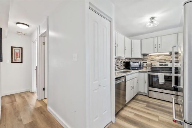 kitchen with light wood-type flooring, backsplash, white cabinets, appliances with stainless steel finishes, and sink