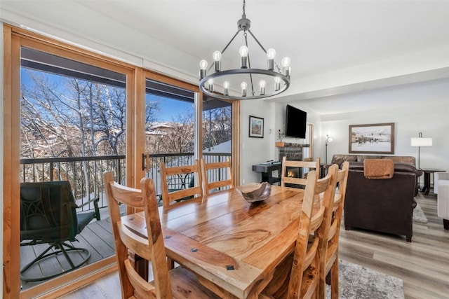 dining space with a chandelier, light wood-type flooring, and a stone fireplace