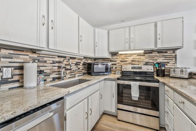 kitchen with appliances with stainless steel finishes, sink, light stone counters, white cabinets, and tasteful backsplash