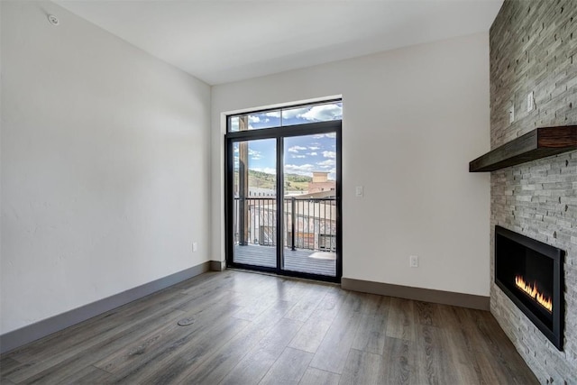 unfurnished living room with wood-type flooring and a stone fireplace