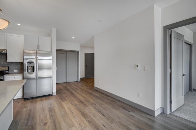 kitchen with appliances with stainless steel finishes, tasteful backsplash, ventilation hood, light hardwood / wood-style flooring, and white cabinets