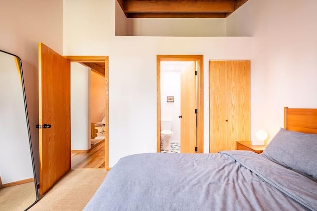 bedroom with beamed ceiling, light colored carpet, and ensuite bath