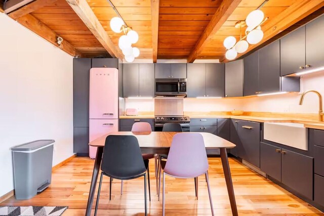 kitchen with sink, beamed ceiling, light wood-type flooring, appliances with stainless steel finishes, and pendant lighting