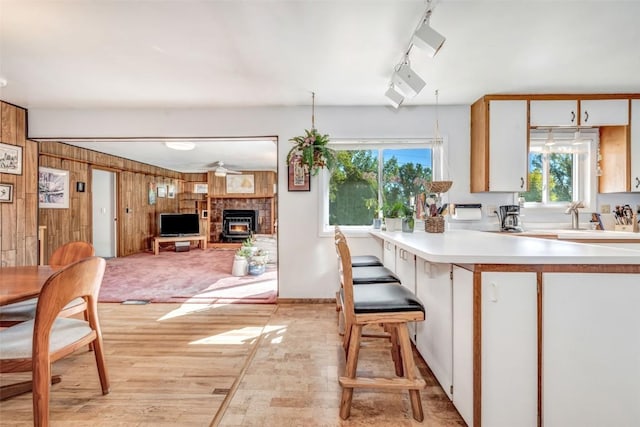 kitchen featuring a breakfast bar, rail lighting, wooden walls, light hardwood / wood-style floors, and white cabinetry