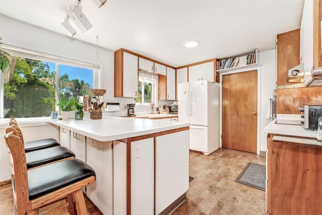 kitchen with pendant lighting, white cabinets, white refrigerator, kitchen peninsula, and a breakfast bar area