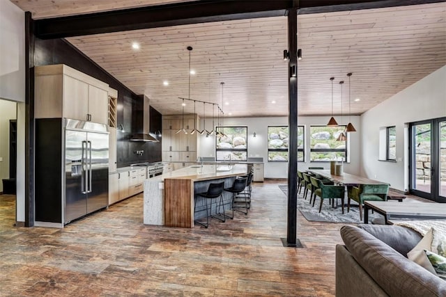 kitchen with a large island, wall chimney exhaust hood, pendant lighting, and built in fridge