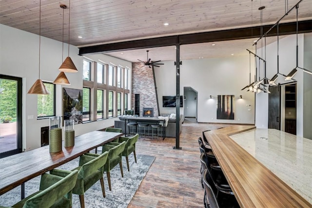 dining space with a towering ceiling, ceiling fan, wooden ceiling, beamed ceiling, and a wood stove