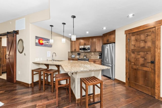 kitchen with a barn door, stainless steel appliances, light stone countertops, kitchen peninsula, and decorative backsplash