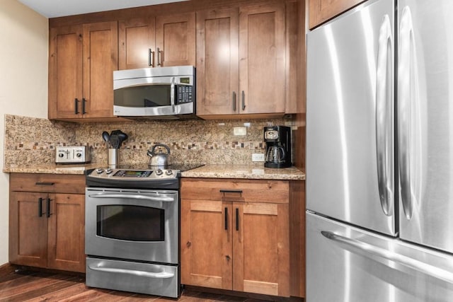 kitchen with stainless steel appliances, dark hardwood / wood-style flooring, decorative backsplash, and light stone counters