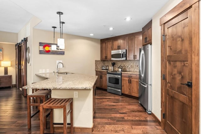 kitchen with a barn door, stainless steel appliances, kitchen peninsula, a breakfast bar, and decorative light fixtures