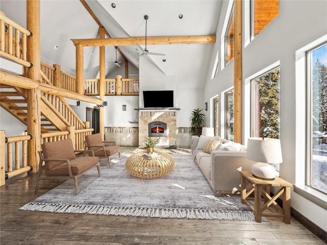 living room with a stone fireplace, hardwood / wood-style floors, high vaulted ceiling, ceiling fan, and beam ceiling