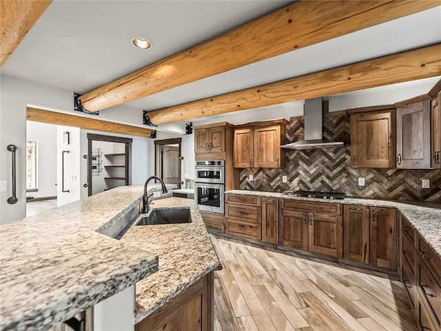 kitchen featuring appliances with stainless steel finishes, sink, light stone counters, beam ceiling, and wall chimney exhaust hood